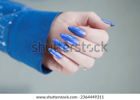 Woman's beautiful hand with long nails and light blue and pink manicure with bottles of nail polish