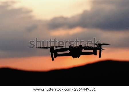 The silhouette of a drone flying over the mountains line at sunset