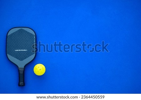 Pickleball tennis racket on the court. Blue background with copy space. Sport court and ball. Royalty-Free Stock Photo #2364450559