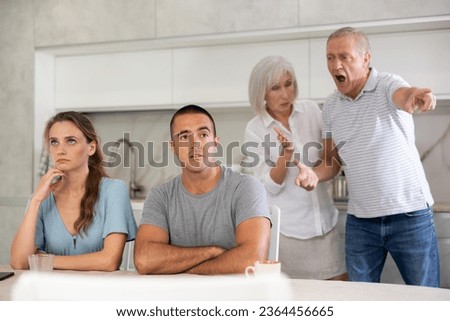 Elderly parents make claims to young couple in home kitchen Royalty-Free Stock Photo #2364456665