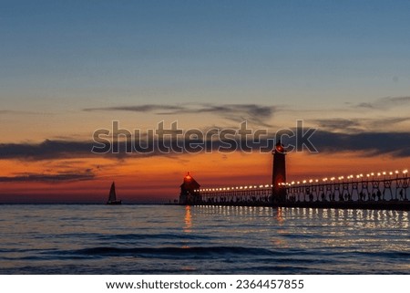 A sailboat approaches the lighthouse in Grand Haven, Michigan, at sunset on Lake Michigan Royalty-Free Stock Photo #2364457855