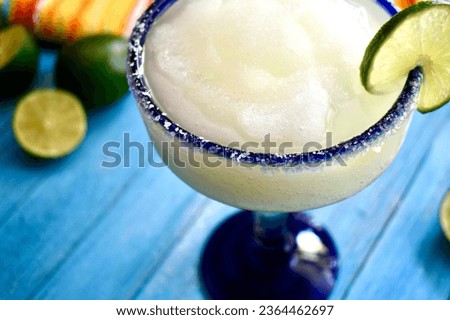 Frozen margarita in a blue rimmed glass with salt and lime slice on a blue wood background