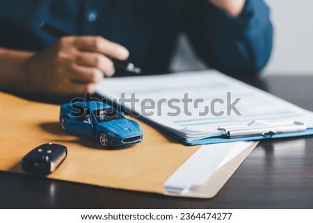 Businesswoman signing car insurance document or lease paper. Writing signature on contract or agreement. Buying or selling new or used vehicle. Car keys on table. Warranty or guarantee.