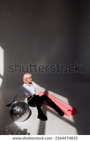 A young woman with pink hair sits elegantly in a minimalist studio, wearing a white blouse, black pants, and leather boots. Modern style and individuality, suitable for fashion and editorial concepts