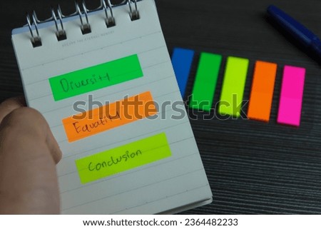 Diversity Equality Conclusion written on colored sticky notes in notebook held by hand on office desk background