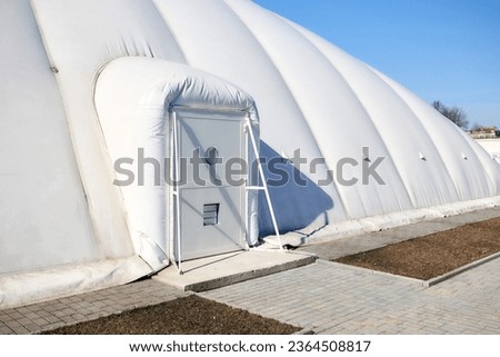 Inflatable air dome stadium. Inflated Tennis air dome or Tennis bubble arena entrance door into structure equipped with airlock either two sets of parallel doors or a revolving door or both. Royalty-Free Stock Photo #2364508817