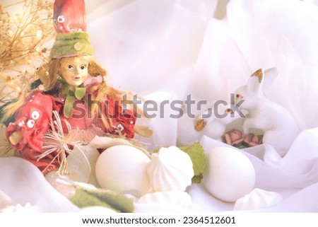 Easter decorations, white eggs, cute elf doll or spring princess, couple of white rabbits,  flowers on white silk with sweet meringue. Easter still life. Sunlight and pastel colors