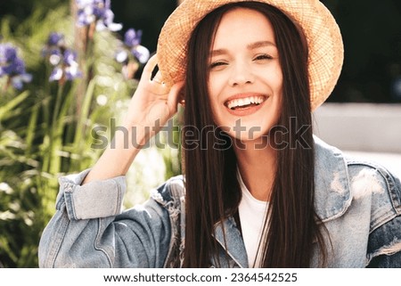 Young beautiful smiling hipster woman in trendy summer jeans jacket clothes. Carefree female posing on the street background at sunny day. Positive model outdoors. Cheerful and happy in hat. Closeup