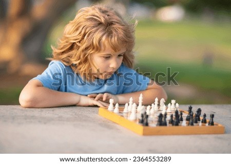 Kid playing chess game in backyard, laying on grass. Concentrated child play chess. Kid playing board game outdoor. Schoolboy chessman thinker. Royalty-Free Stock Photo #2364553289