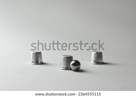 Metal thimbles and ball on light grey background. Thimblerig game Royalty-Free Stock Photo #2364555115