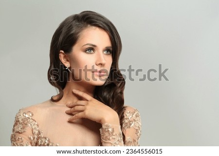 Beautiful woman with makeup and stylish dark hair wearing silver earring on grey background