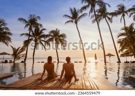 couple on the beach at sunset, honeymoon travel, man and woman sitting near swimming pool in hotel resort Royalty-Free Stock Photo #2364559479