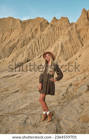 beautiful young woman with long blond hair in a hat against the backdrop of a sandy desert landscape Royalty-Free Stock Photo #2364559701
