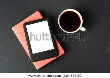 Composition with modern e-book reader, hardcover book and cup of coffee on table