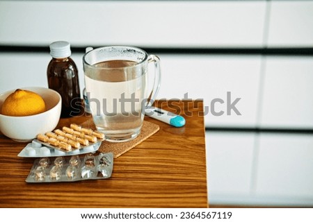 Natural and medical cold and flu remedies on table at home. Cold and flu influenza fall autumn and winter season. Cup with hot tea, lemon, thermometer pills and capsules Royalty-Free Stock Photo #2364567119
