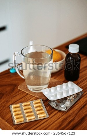 Natural and medical cold and flu remedies on table at home. Cold and flu influenza fall autumn and winter season. Cup with hot tea, lemon, thermometer pills and capsules