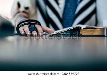 Young man practicing the reading of the Torah prior to Bar Mitzvah celebration. wearing Tefillin on the right hand. Royalty-Free Stock Photo #2364569723