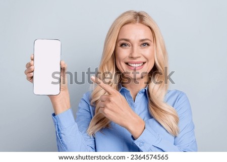 Photo of charming cheerful girl indicate finger empty space smart phone screen offer isolated on grey color background