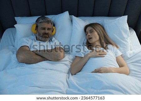 Irritated man with headphones lying near his snoring wife in bed at home Royalty-Free Stock Photo #2364577163