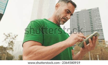 Mature man wearing casual clothes, standing on modern buildings background, texting on smartphone