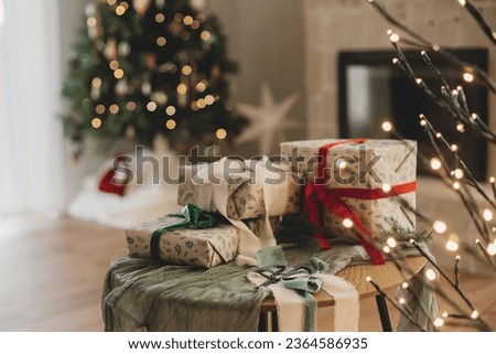Stylish wrapped christmas gifts with ribbon on table on background of decorated christmas tree with vintage baubles, rustic fireplace and festive lights. Merry Christmas and Happy Holidays!