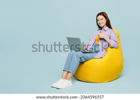 Full body young happy IT woman she wear purple shirt yellow t-shirt casual clothes hold use work point on laptop pc computer isolated on plain pastel light blue background studio. Lifestyle concept