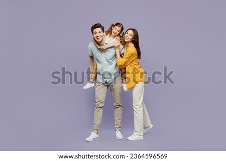 Full body young joyful happy parents mom dad with child kid daughter girl 6 years old wear blue yellow casual clothes giving piggyback ride to joyful, sit on back isolated on plain purple background Royalty-Free Stock Photo #2364596569