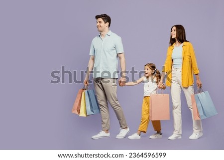 Full body side view young happy parents mom dad with child daughter girl 6 years old wear yellow casual clothes hold shopping bags go isolated on plain purple background. Black Friday sale day concept