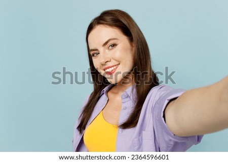 Close up young happy woman wears purple shirt yellow t-shirt casual clothes doing selfie shot pov on mobile cell phone isolated on plain pastel light blue background studio portrait. Lifestyle concept