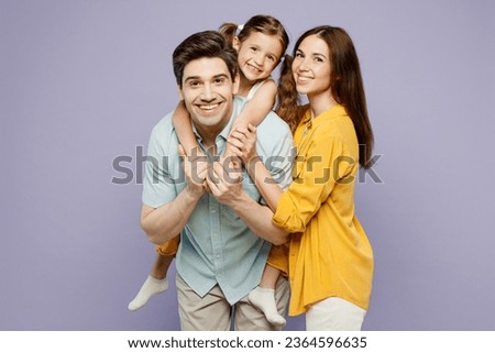 Young cool parents mom dad with child kid daughter girl 6 years old wear blue yellow casual clothes give piggyback ride to joyful, sit on back isolated on plain purple background. Family day concept