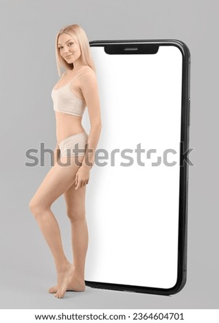 Slim woman in underwear and big smartphone on grey background. Weight loss concept