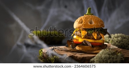 Halloween Burger banner. Halloween party creative burger concept with big beef patties with pumpkin head rolls, tomato and pepper on wooden board on dark background with moss. Copy space for text