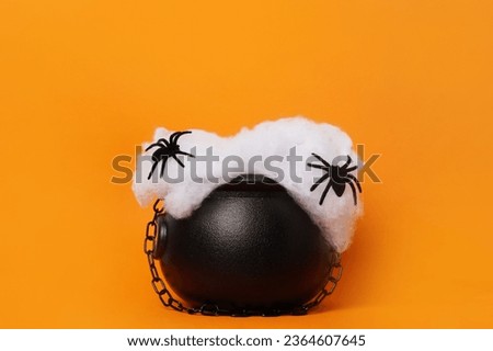Happy Halloween holiday concept. Witch's cauldron with black spiders on orange background, copy space. Witch's cauldron as a pedestal for products Royalty-Free Stock Photo #2364607645