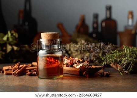 Essential herbal tincture in a small glass bottle. On a table dried herbs, flowers, spices, and old kitchen utensils. Alternative or complementary medicine treatment. Royalty-Free Stock Photo #2364608427