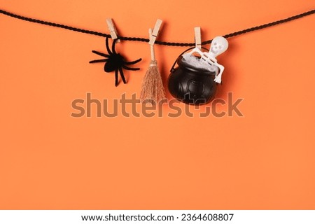 Creative Halloween card with witch set spider, broom and skeleton on the rope, orange background. copy space