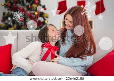 Festive mother and daughter on the couch with gift against hanging decorations
