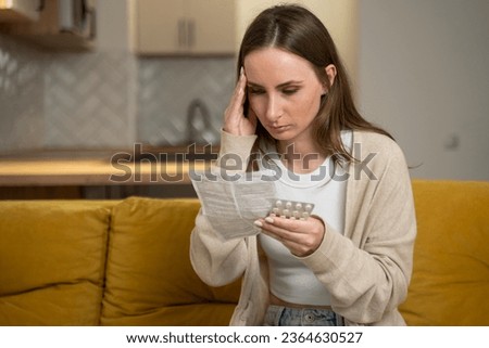 Beautiful young woman with pills and instructions at home sitting on a yellow sofa.  Royalty-Free Stock Photo #2364630527