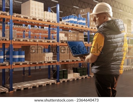 Man in warehouse. Logistics center employee. Worker with laptop in warehouse. Man inspects warehouse racks. Barrels and boxes are stored on pallets. Businessman with laptop in storage building Royalty-Free Stock Photo #2364640473