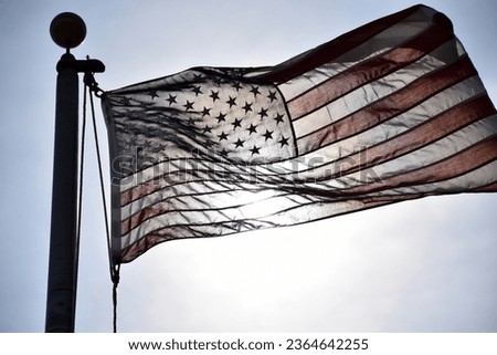United States of America flag on a flag pole that is backlight. The sun is shinning through the material of the flag making a unique image. 