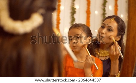 South Indian woman in traditional wear helping her daughter to get ready for the celebration of Diwali - lifestyle Family. Beautiful mother teaching her young daughter how to use a makeup brush - m... Royalty-Free Stock Photo #2364644537
