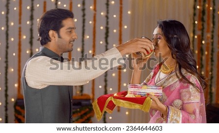 Newly wed couple celebrating their first Karwa Chauth together - Indian festival. Good looking husband performing Karwa Chauth traditions of offering water to her fasting wife in traditional wear -... Royalty-Free Stock Photo #2364644603