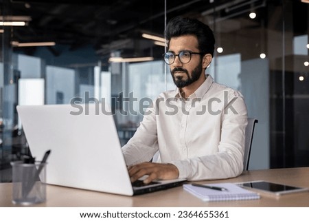 Serious young Indian businessman man working focused on laptop while sitting in office at desk. Royalty-Free Stock Photo #2364655361