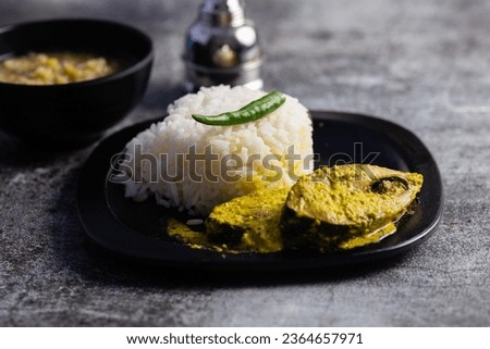 Hilsa fish curry with mustard paste and green chilli served on plate along side rice with selective focus