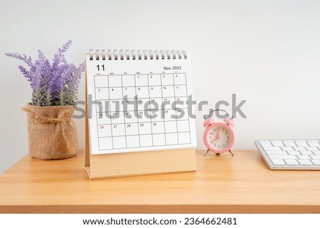 November 2023, Monthly desk calendar for 2023 year on wooden table with pink alarm clock.