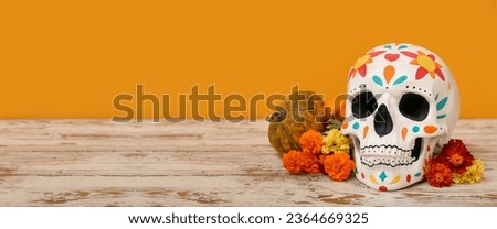 Painted human skull for Mexico's Day of the Dead (El Dia de Muertos), pumpkin and flowers on table against orange background with space for text