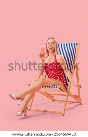 Beautiful young woman with soda relaxing in deck chair on pink background