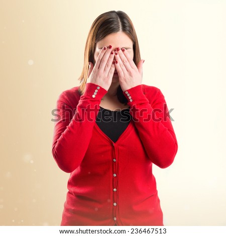 young girl covering her eyes over ocher background 