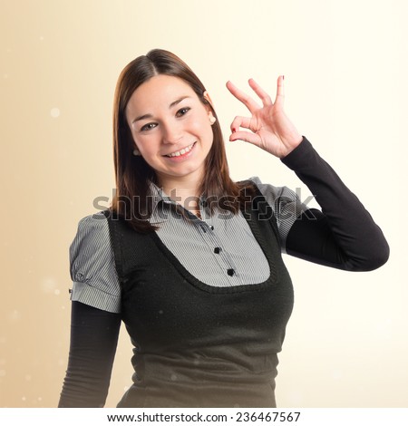 Young woman making Ok sign over ocher background 