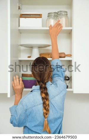 Woman opening kitchen cupboard with ingredients and set of kitchen utensils for bakery Royalty-Free Stock Photo #2364679503