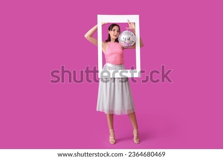 Beautiful young woman with disco ball and frame on purple background